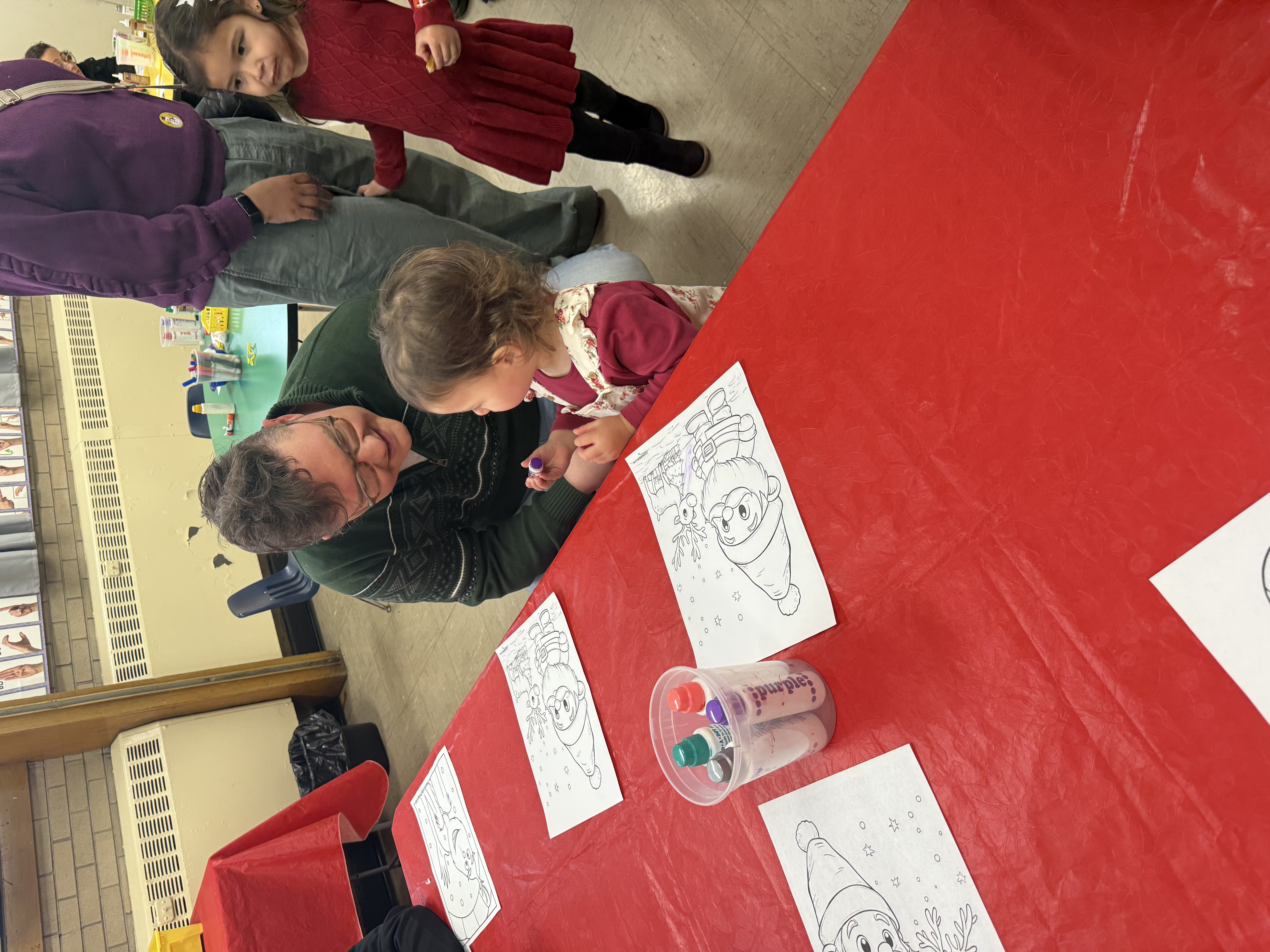 Photo of dad and young child coloring at red table.